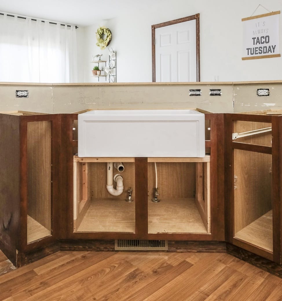 a white fireclay kitchen sink in a standard kitchen with cabinet doors off