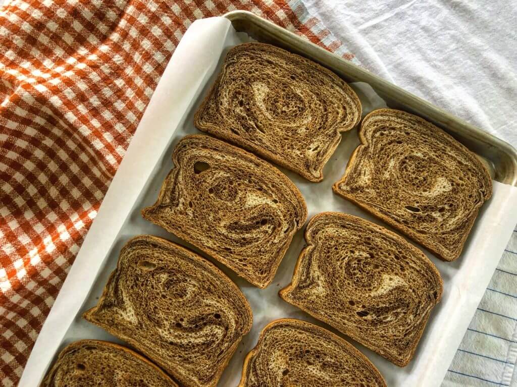 Slices of rye bread arranged on a baking sheet lined with parchment paper.