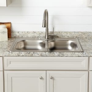 Dated stainless steel drop-in kitchen sink with nickel faucet in tan cabinets with formica countertop.