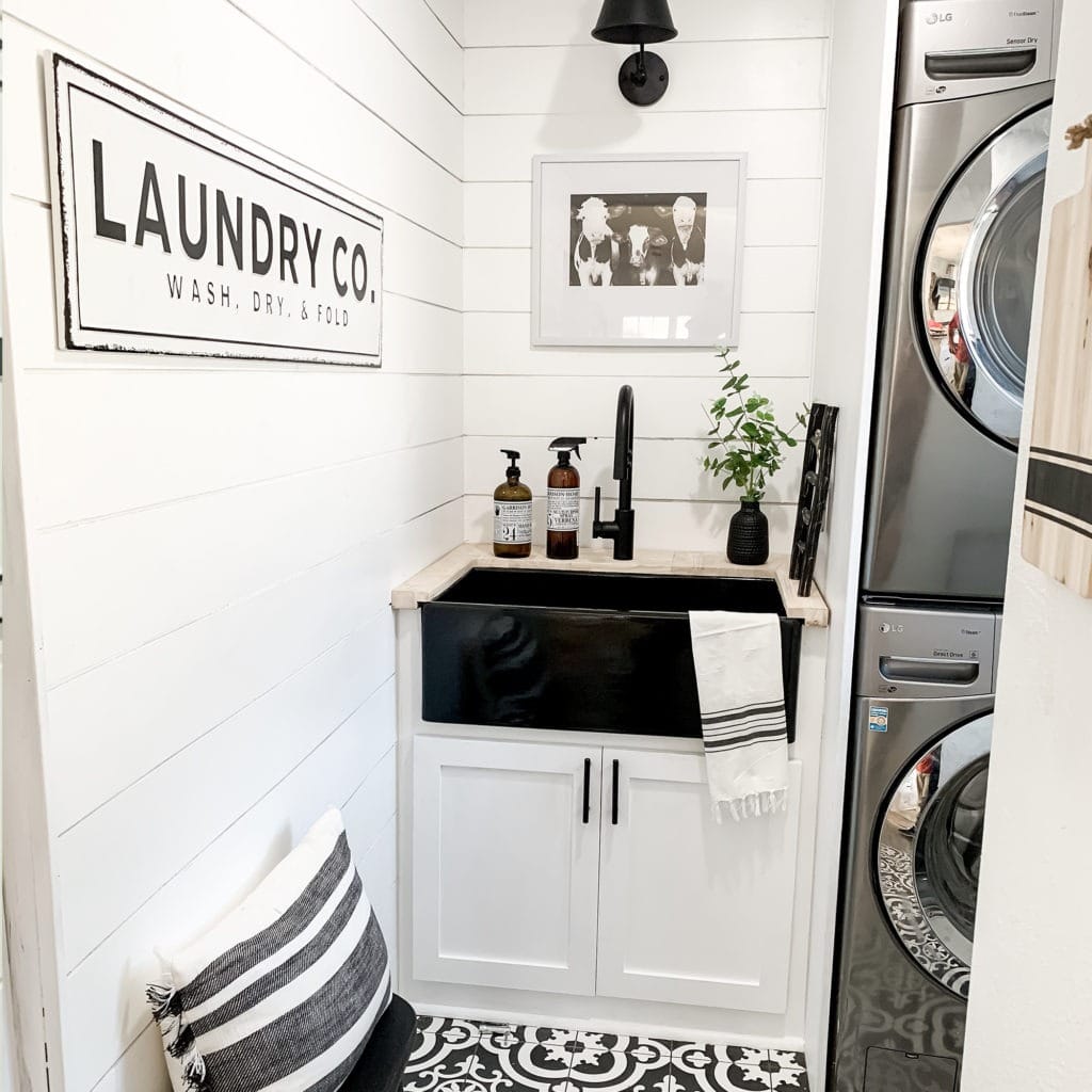 A glossy black rectangular undermount farmhouse sink made in fireclay in a modern black and white laundry room.