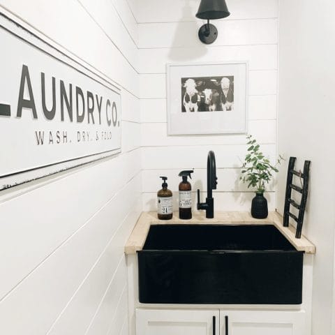 A glossy black rectangular undermount farmhouse sink made in fireclay in a modern black and white laundry room.