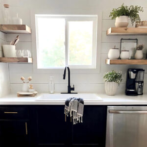 Contemporary kitchen with black cabinets and white countertop with fireclay drop-in sink and black faucet infront of a window