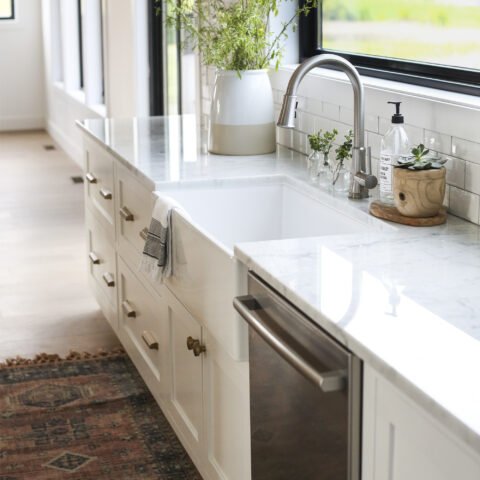 White farmhouse kitchen sink with a brushed nickel faucet in front of a window