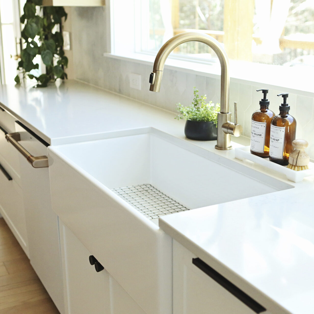 White farmhouse kitchen sink with a gold faucet in front of a window