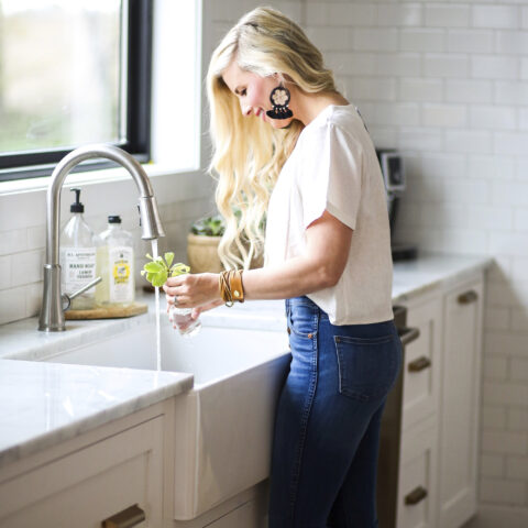 Woman filling a glass of water in her farmhouse sink in front of a window