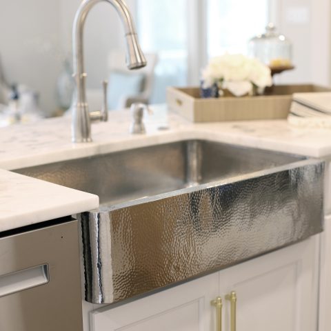 A hand hammered polished stainless steel rectangular undermount farmhouse sink in a home kitchen.