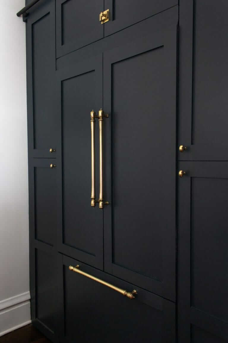 A dark kitchen cabinet with large brass handles and hardware, designed to blend seamlessly with the surrounding cabinetry.