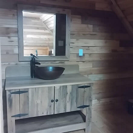 Rustic bathroom with wood-paneled walls, featuring a wooden vanity with a dark vessel sink and matching faucet, and a framed mirror above.