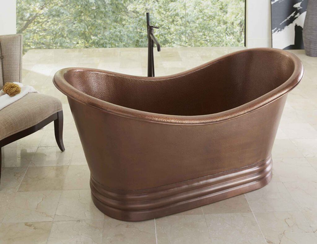 Euclid copper freestanding tub in large bathroom with window with view of greenery outside.