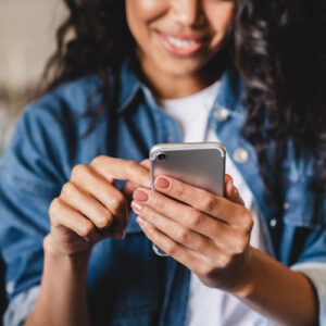 Smiling african american woman using smartphone at home, shopping online, while relaxing on couch